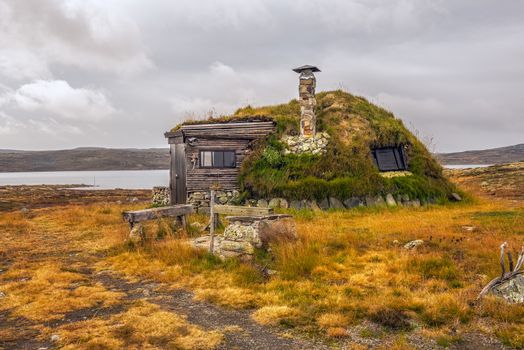 Cabin with turf roof near Hardangervidda National Park with a lake in the background, Hordaland county, Norway.
