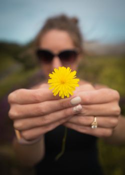 A portrait of a woman holding a yellow dandelion flower close up