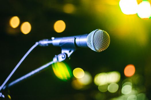 singer's vocal microphone stands on stage during a concert with multi-colored lights on the background