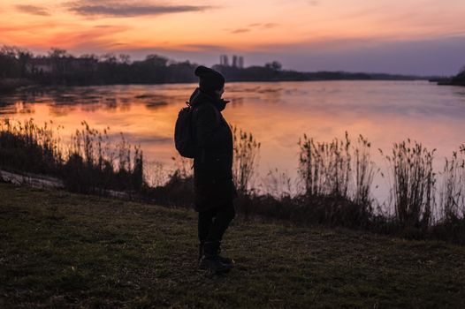 silhouette of a human on the background of a lake in the forest looking at a beautiful sunset