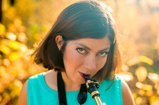 portrait of a cute young saxophonist woman with black hair in blue clothes on a yellow background