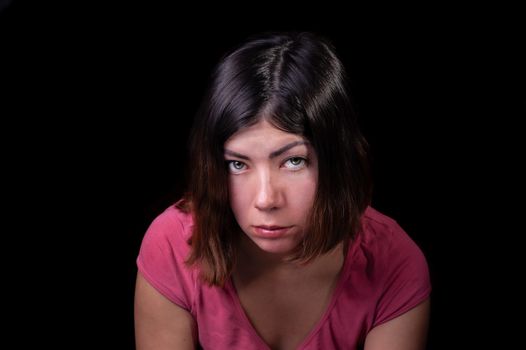 beautiful dark-haired girl with green eyes in a pink t-shirt with a serious sad look on an isolated black background
