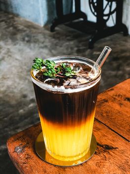 Iced fresh orange juice topped with espresso on wooden table in Modern cafe