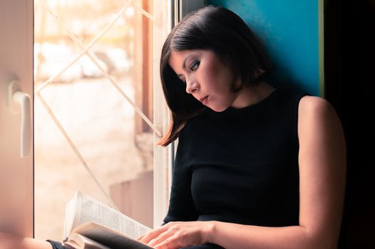 gorgeous young brunette woman in black clothes is reading a book