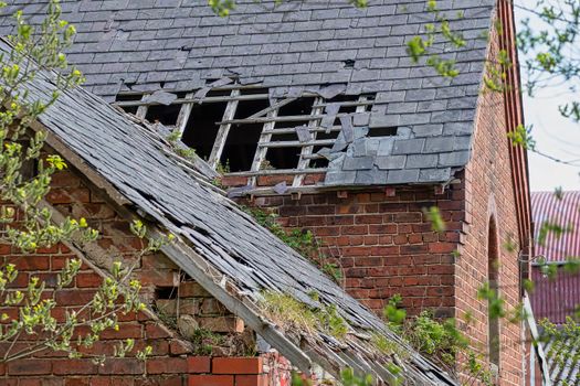 Damaged slate roof tiles on a pitched roof on a derelict house