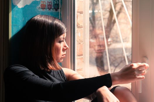 upset young beautiful brunette girl in black clothes looking out the window