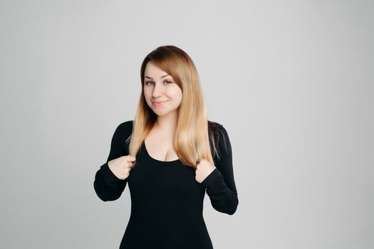 Studio portrait of beautiful blondy woman with perfect cared and long hair after beauty salon. Girl in black wear smiling at camera, posing against gray background. Beauty and health.