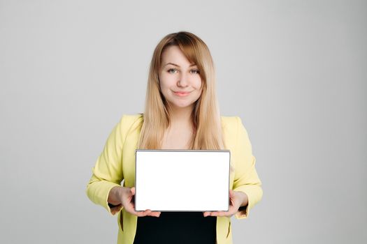 Portrait of blonde haired woman, wearing in yellow jacket and black blouse, holding tablet computer and showing at camera. Positivity girl posing against gray studio background. Concept of business.