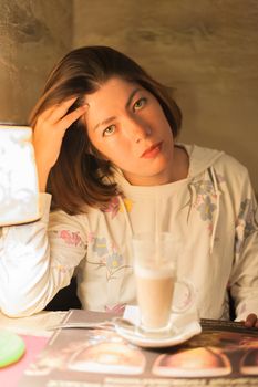 nice young brunette girl sitting at a table near a glass of latte macchiato