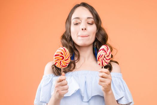 Front view of stylish female teenager wearing tracksuit and hat chewing gum and keeping big blue balloon in studio. Young girl looking at camera and posing on grey isolated background.