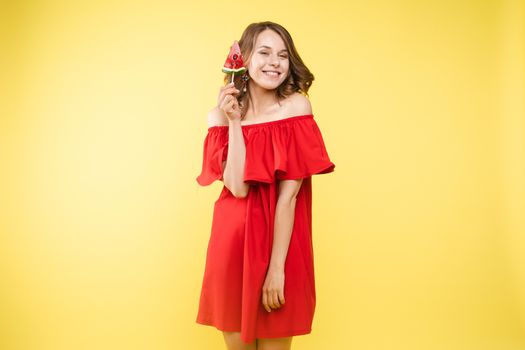 Beautiful and seductive woman wearing like sweet doll, posing at studio with candy on stick. Confident pretty woman in dress andsunglasses, holding hand on waist. Fashion, glamour.