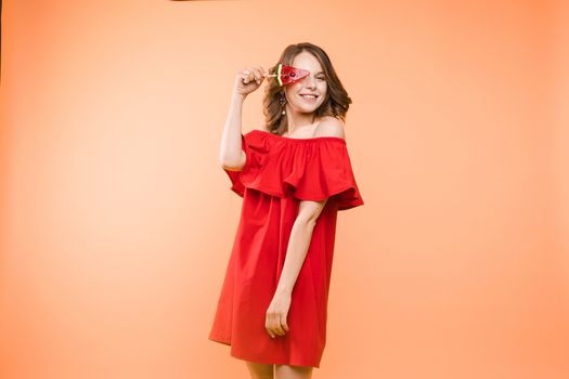 Close up portrait of attractive lovely girl in light dress handing lolipop isolated on yellow background