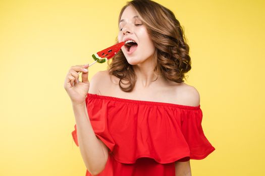 Beautiful and seductive woman wearing like sweet doll, posing at studio with candy on stick. Confident pretty woman in dress andsunglasses, holding hand on waist. Fashion, glamour.