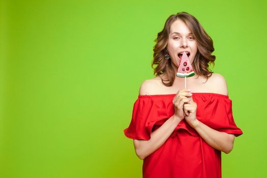 Beautiful and seductive woman wearing like sweet doll, posing at studio with candy on stick. Confident pretty woman in dress andsunglasses, holding hand on waist. Fashion, glamour.