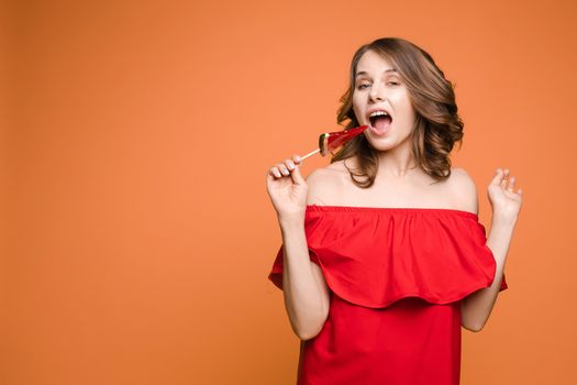 Close up portrait of attractive lovely girl in light dress handing lolipop isolated on yellow background