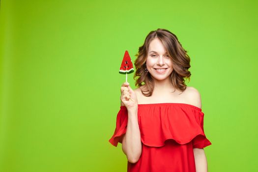 Beautiful and seductive woman wearing like sweet doll, posing at studio with candy on stick. Confident pretty woman in dress andsunglasses, holding hand on waist. Fashion, glamour.