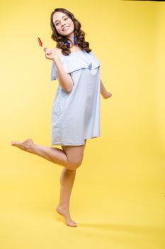 Full length isolate portrait of positive brunette young girl in jeans and t-shirt and sneakers jumping over yellow background. She is smiling at camera.