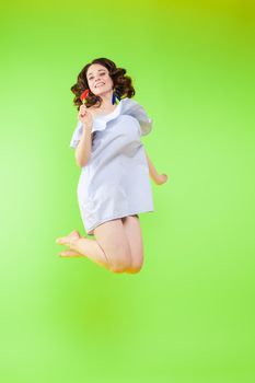 Full length isolate portrait of positive brunette young girl in jeans and t-shirt and sneakers jumping over yellow background. She is smiling at camera.