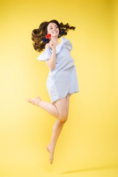 Full length isolate portrait of positive brunette young girl in jeans and t-shirt and sneakers jumping over yellow background. She is smiling at camera.