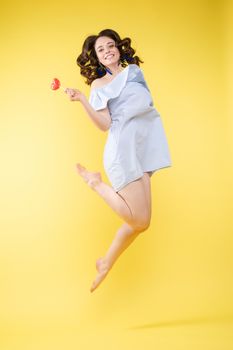 Full length isolate portrait of positive brunette young girl in jeans and t-shirt and sneakers jumping over yellow background. She is smiling at camera.