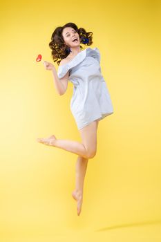 Full length isolate portrait of positive brunette young girl in jeans and t-shirt and sneakers jumping over yellow background. She is smiling at camera.