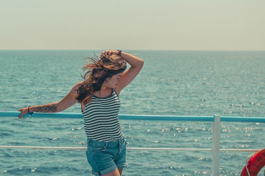 lovely young black-haired girl in a striped T-shirt and blue shorts posing on the deck of a ship on the high seas