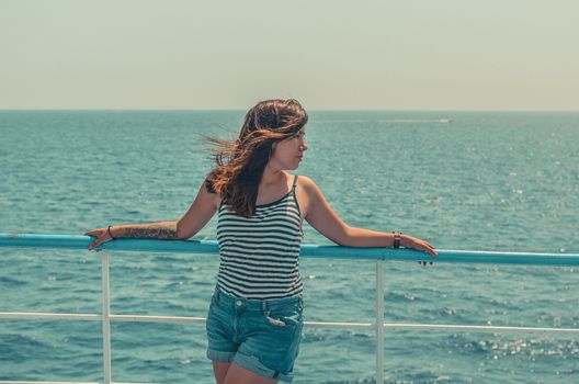 pretty young woman in striped t-shirt and blue denim shorts enjoys the sea on the deck of a ship