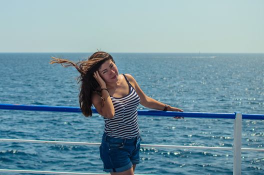 beautiful young black-haired girl in a striped T-shirt posing leaning on a railing near the sea