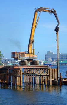 A hydraulic pile driver sinks a large support post into the river bed for bridge construction.
The letters in the back say port.
