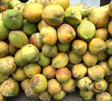 Large clusters of coconuts are stored on the sidewalk of a coconut water stand