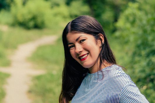 young beautiful smiling girl walks in a summer Park with green leaves