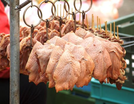 Large pieces of raw chicken meat are put on metal skewers for a barbeque