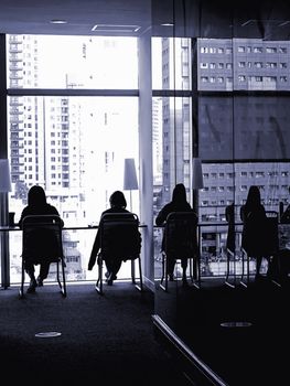 Monochrome image of outline of people reading by a large glass building facade
