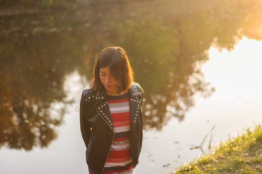 pretty teenager girl with black hair posing on a background of a forest lake in the sunshine
