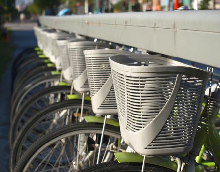 A row of green rental bicycles with gray baskets