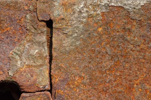 A large iron plate with a hole that is heavily corroded by rust
