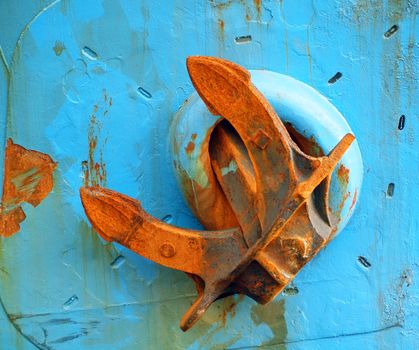 A massive anchor with rust is fastened on the side of a blue ship
