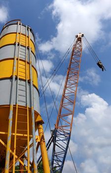 A large grey and yellow cement silo and a crane are set up at a construction site