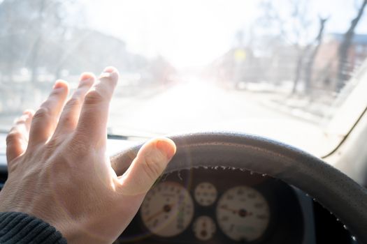 The hand of the driver of the car covers the sunlight, which blinds the person to see the road situation