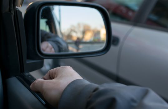 a man's hand on the car door on the background of a female silhouette in the mirror of the rear view mirror