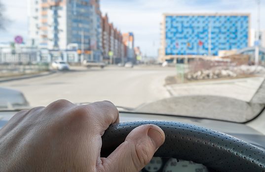 the driver hand on the steering wheel of a car that passes on the highway against the background of city buildings and office centers