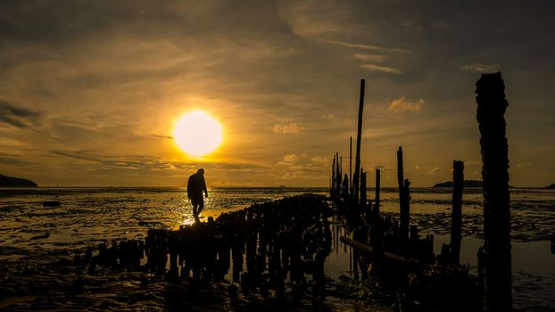 Silhouette of man walking on the beach at sunrise , beautiful cloudy sky reflected on the beach.