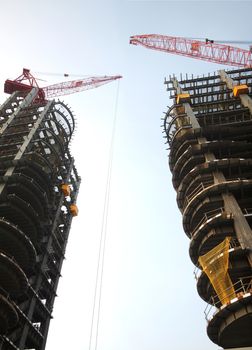 Two cranes works between two half finished high rise buildings
