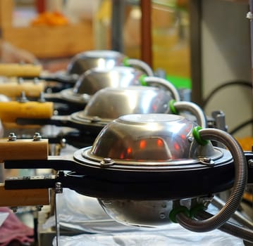 An outdoor food vendor uses a row of waffle irons

