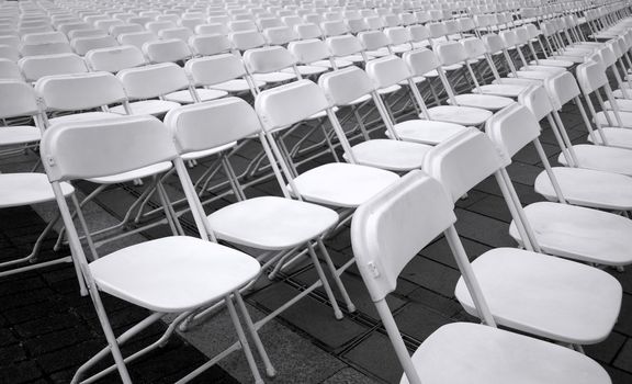 Plastic folding chairs are set up for an outdoor concert
