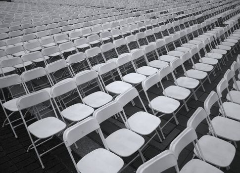 Row after row of plastic chairs are set up for an outdoor concert
