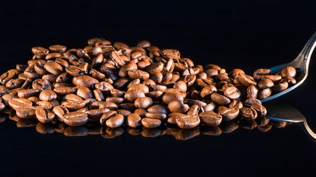 Coffee beans on a black mirror background close-up with a coffee spoon.