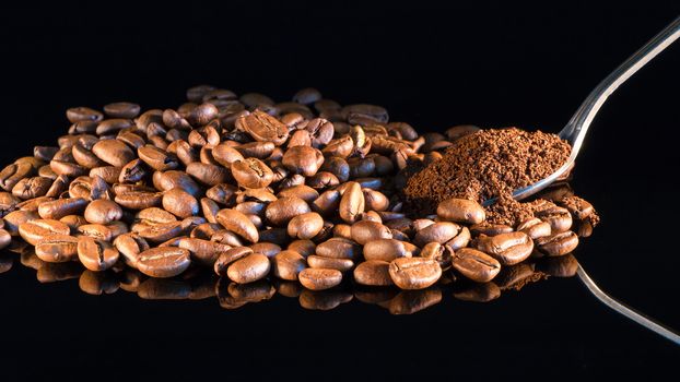 Coffee beans on a black mirror background close-up with a spoon of ground coffee.