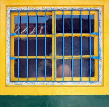 An old window with yellow frames and blue iron bars
