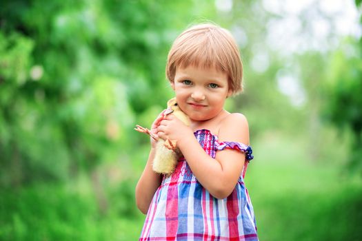 Happy little girl in a summer sundress hugs a duckling standing on the nature in the grass